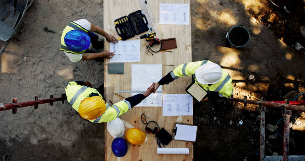 Poignée de main sur un chantier avec plans et outils